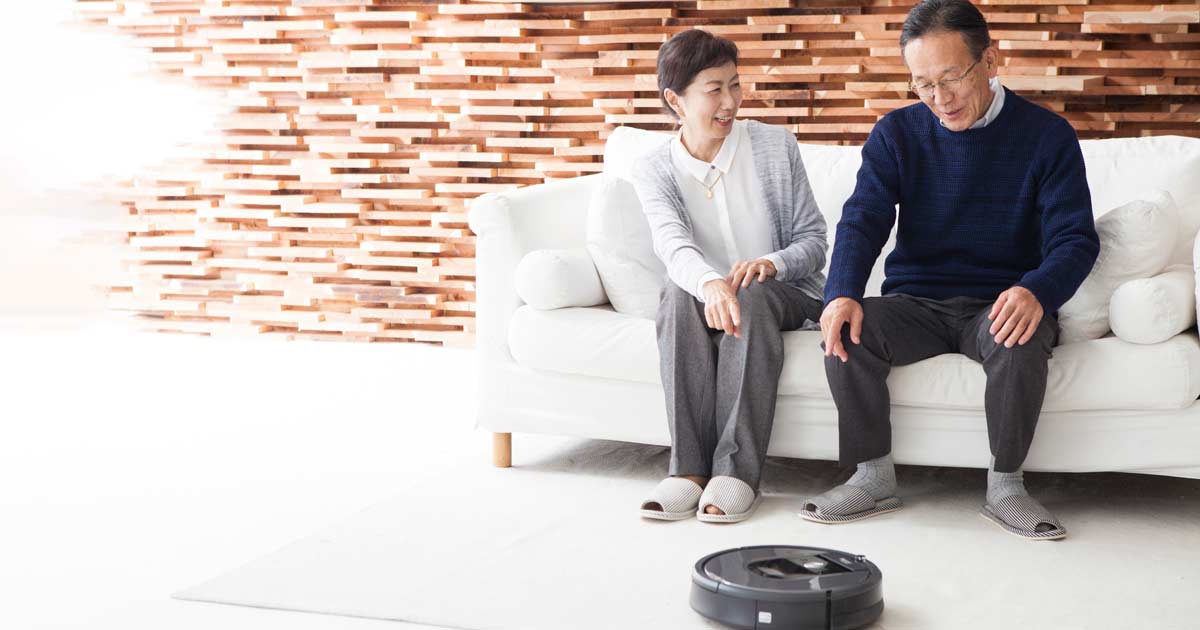 Senior couple sitting on couch watching their Roomba vacuum