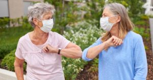 Two senior women wearing face masks touching elbows to greet each other