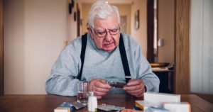 Senior man sitting at diing room table having difficulty with his medications