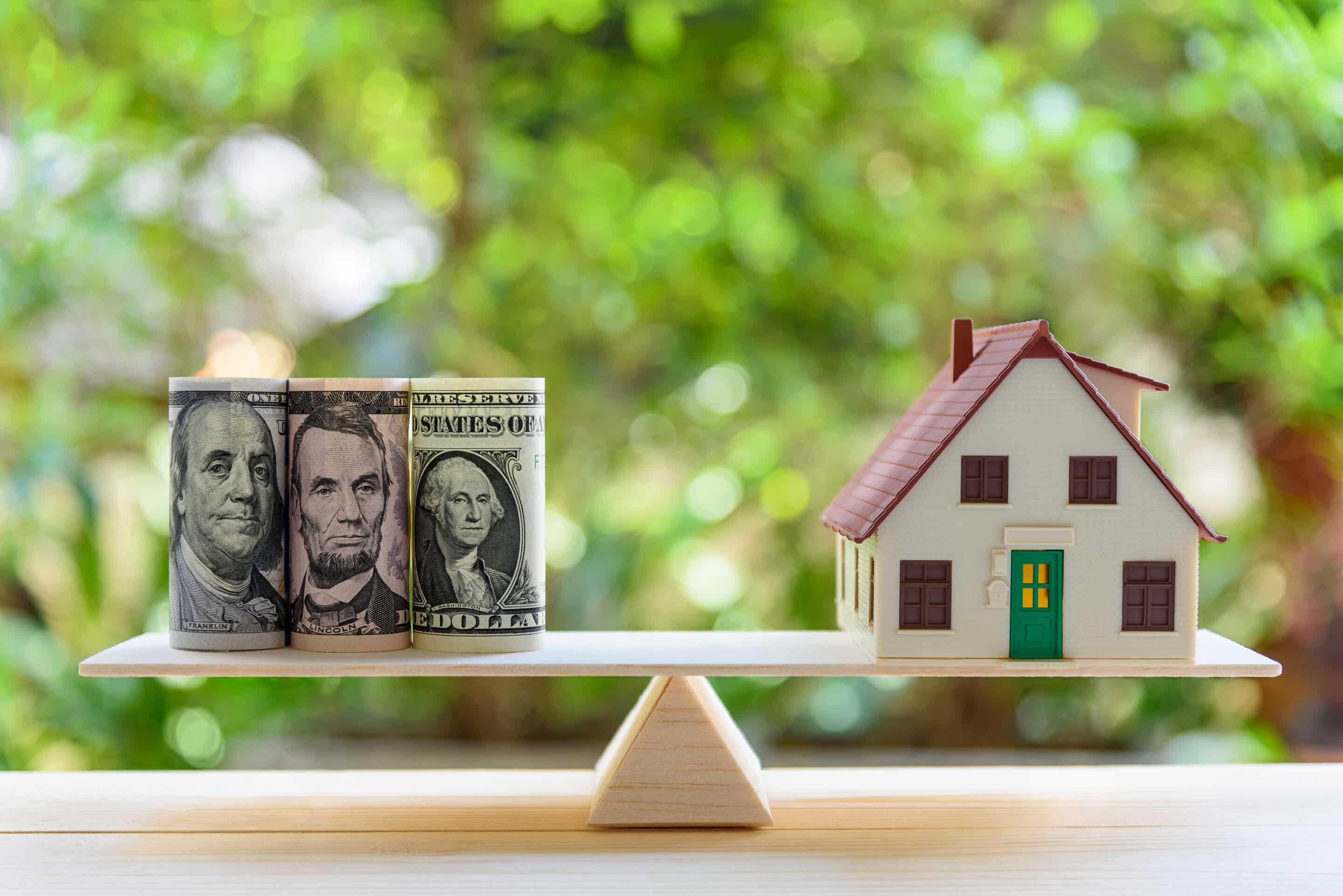 Home loan / reverse mortgage or transforming assets into cash concept : House model, US dollar notes on a simple balance scale, depicts a homeowner or a borrower turns properties / residence into cash reverse mortgage